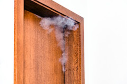 Rauch und Brandgase steigen an einer Holztür auf und können Brandgeruch sowie Rauchgasablagerungen verursachen.